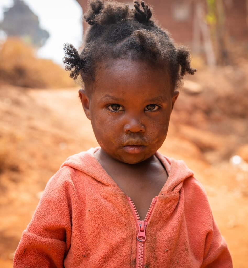 Poor little girl wearing dirty clothes in an African village, poverty and crisis concept.
